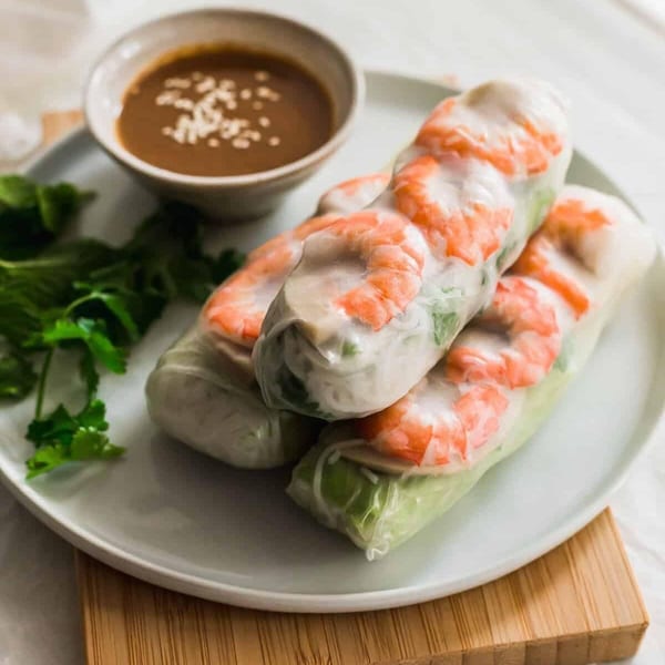 Three fresh shrimp spring rolls with herbs and noodles, served with peanut dipping sauce.