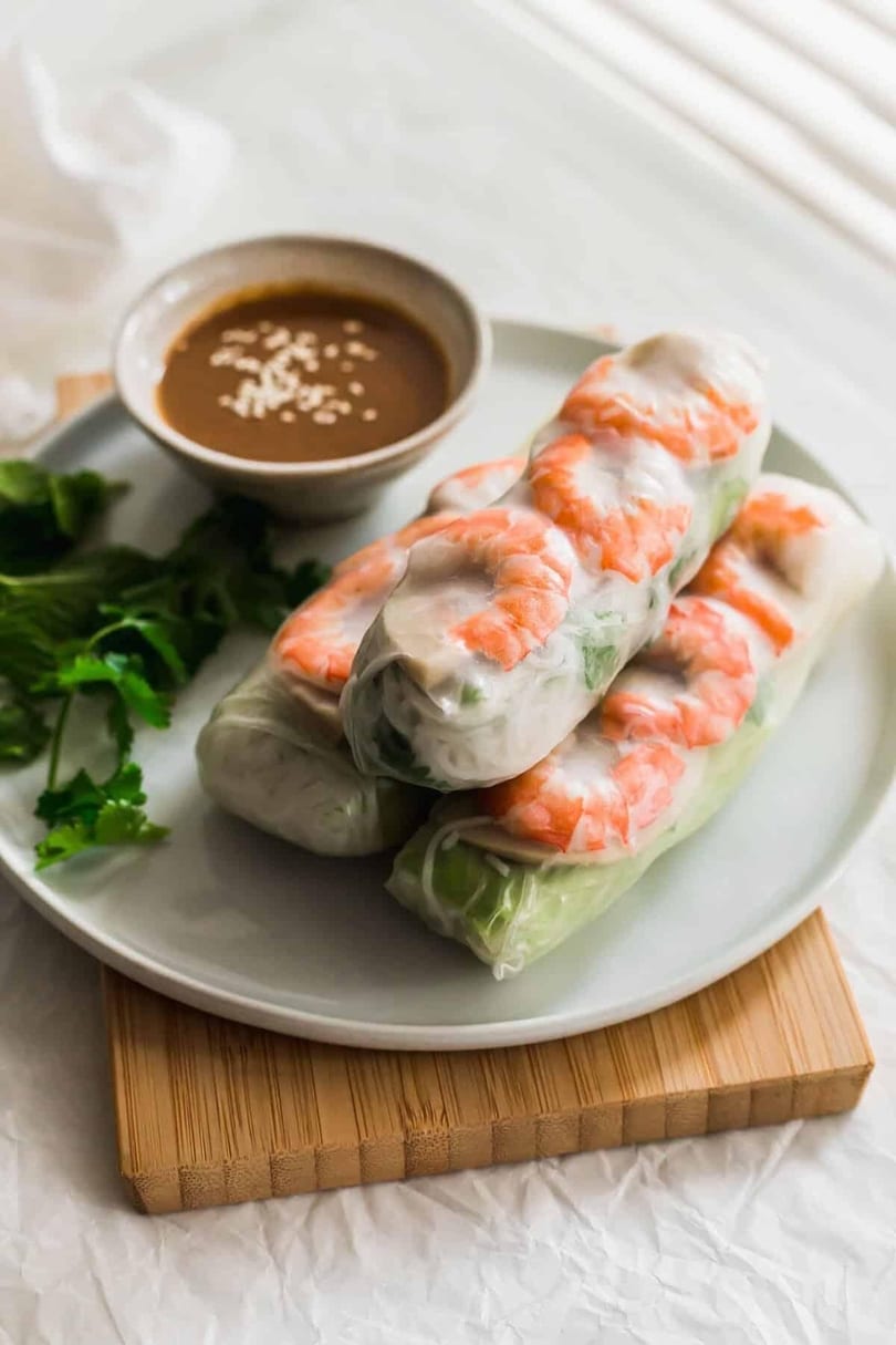 Three fresh shrimp spring rolls with herbs and noodles, served with peanut dipping sauce.